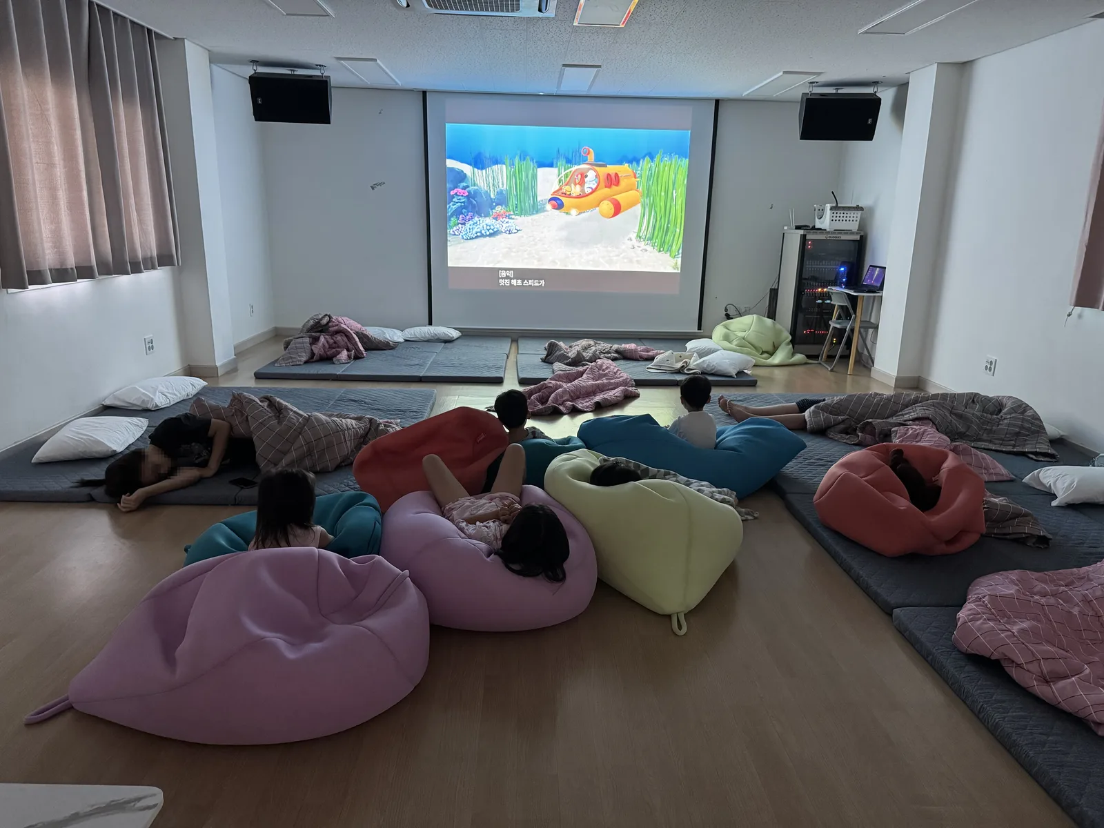 빔프로젝터로 뽀로로를 보는 아이들과 빈백 소파 (얼굴 모자이크 처리)